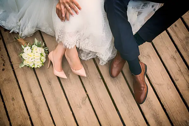 Fotografía de primer plano de las manos entrelazadas de la novia y el novio, mostrando los anillos de boda y los detalles delicados de las flores y el encaje.